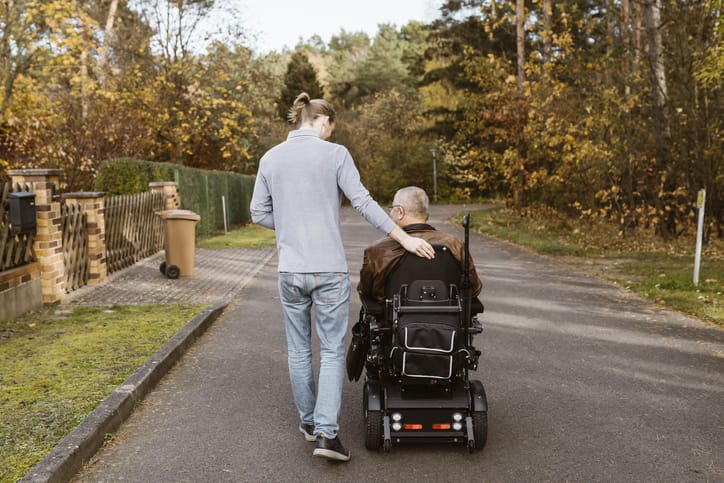 Photo shows a caregiver walking with a man in a wheelchair/Getty Images