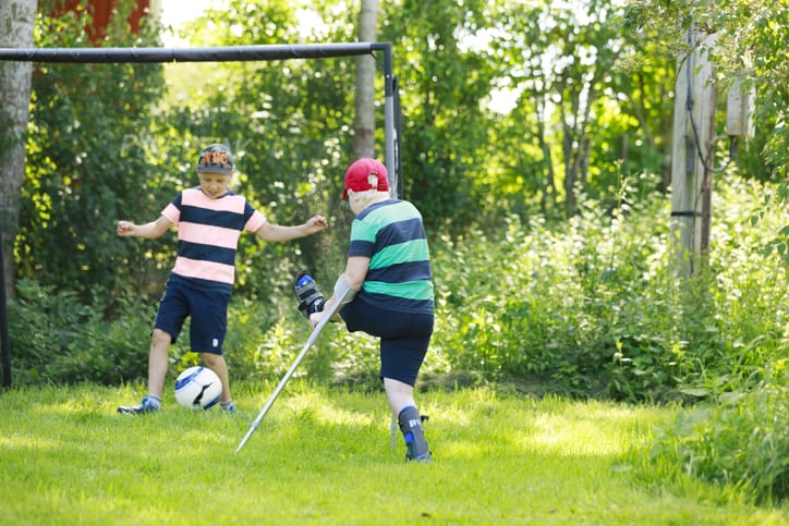 Photo of two boys playing soccer, one with crutches
