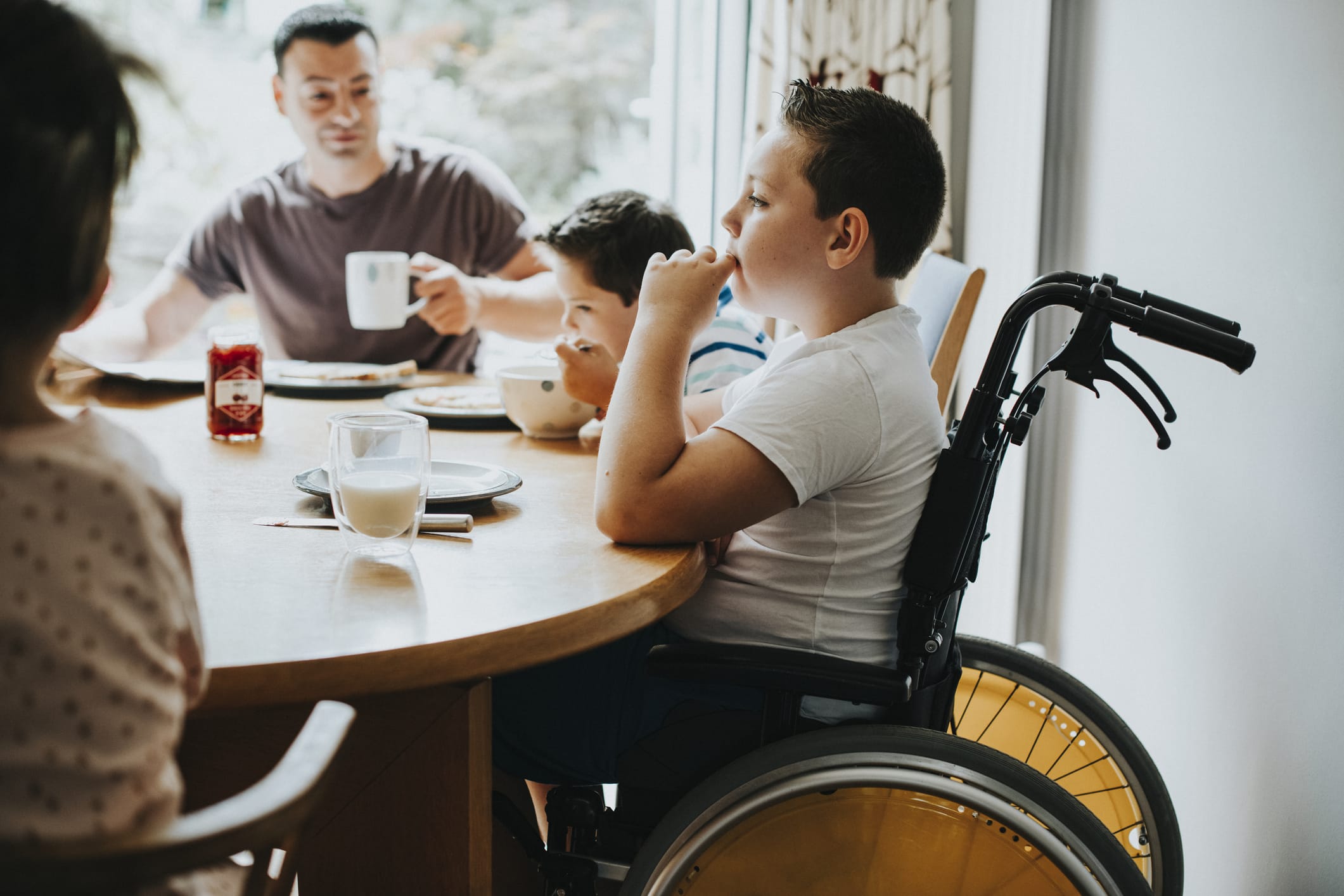Boy in wheelchair eating breakfast with his family