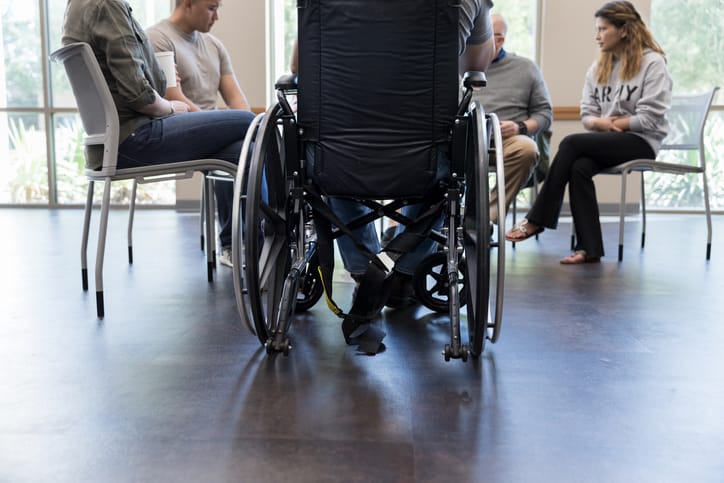Photo shows a man in a wheelchair participating in a support group meeting/Getty Images