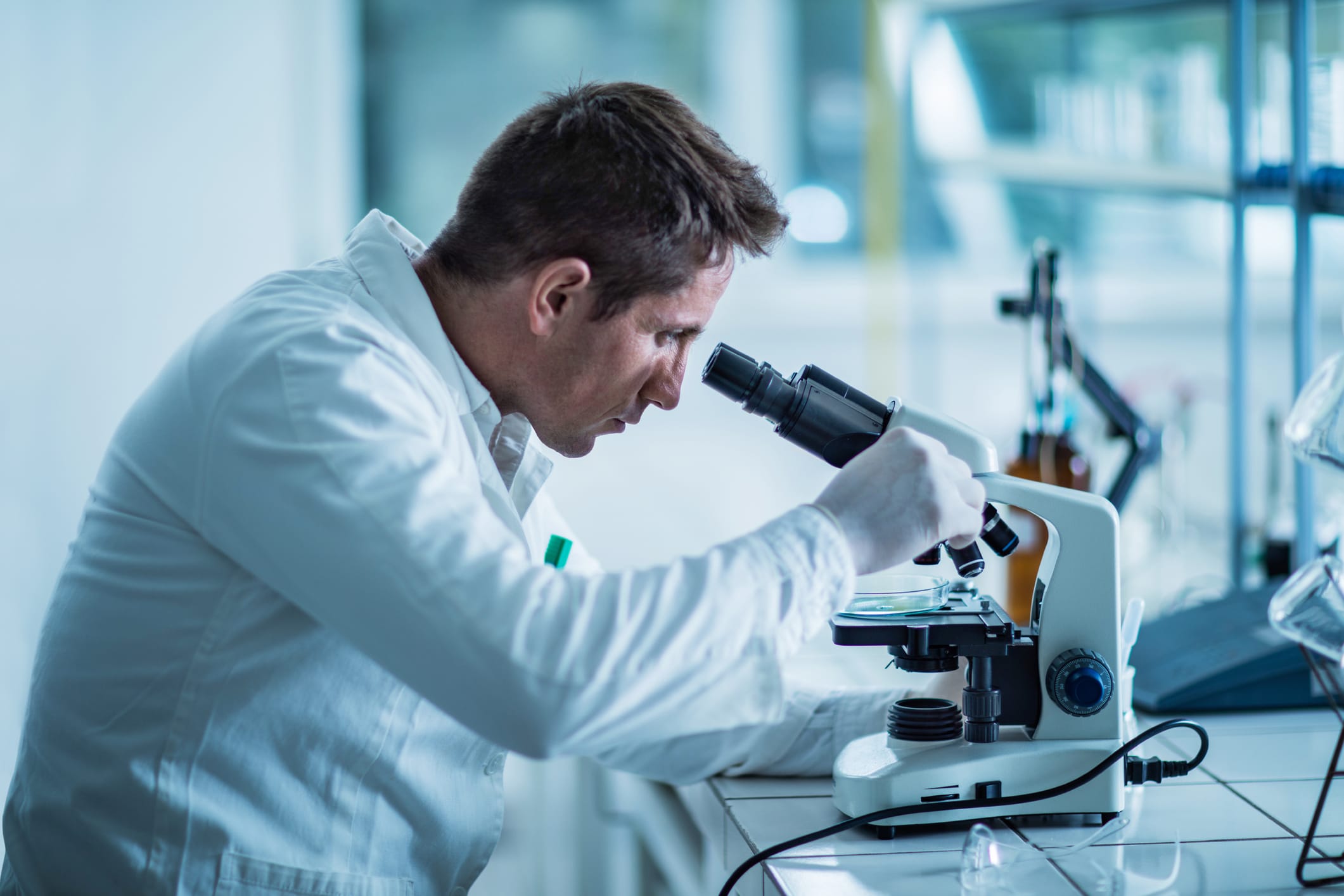 Scientist in lab coat looking at sample under a microscope