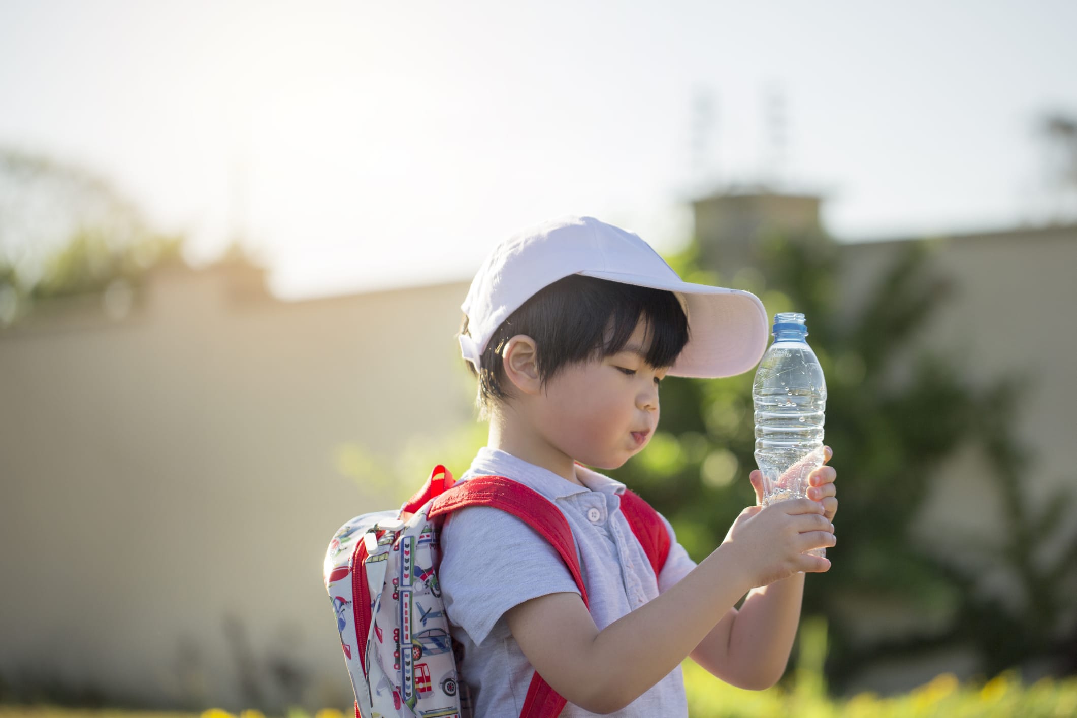 Young boy wearing a backpack holding a water bottle up