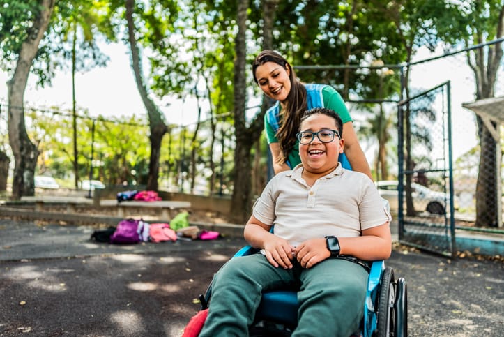 Boy in wheelchair in the school yard with teacher