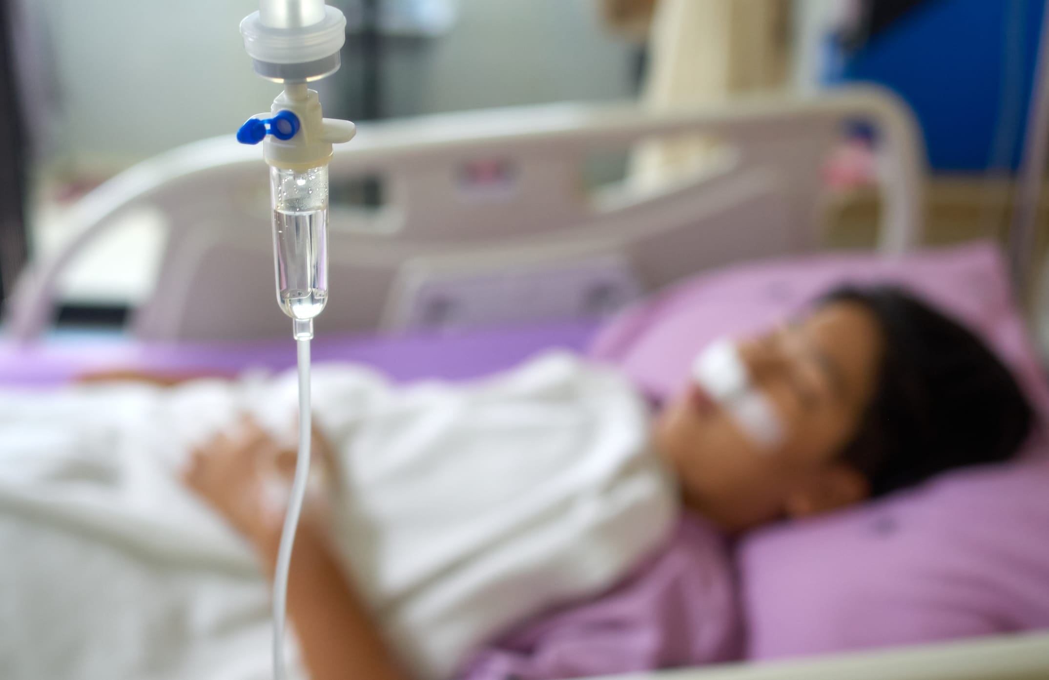 A patient resting on the bed in the hospital ward with an IV in foreground