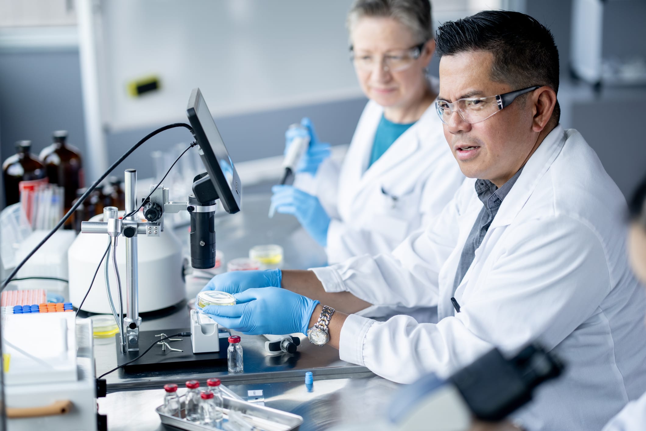 A female medical laboratory technician works independently as she draws plasma samples from a a vile and analyzes them. She is wearing a lab coat as well as protective eyewear and gloves as she focuses on her task.