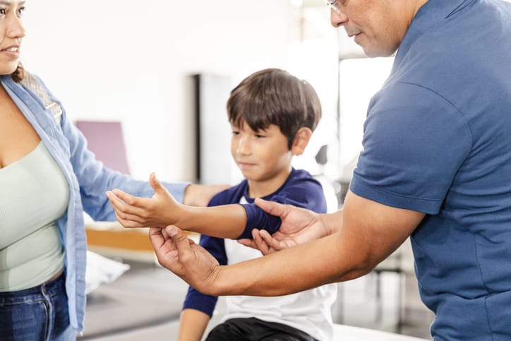 The mid adult mother watches the occupational therapist's face as he examines her son's injured arm.
