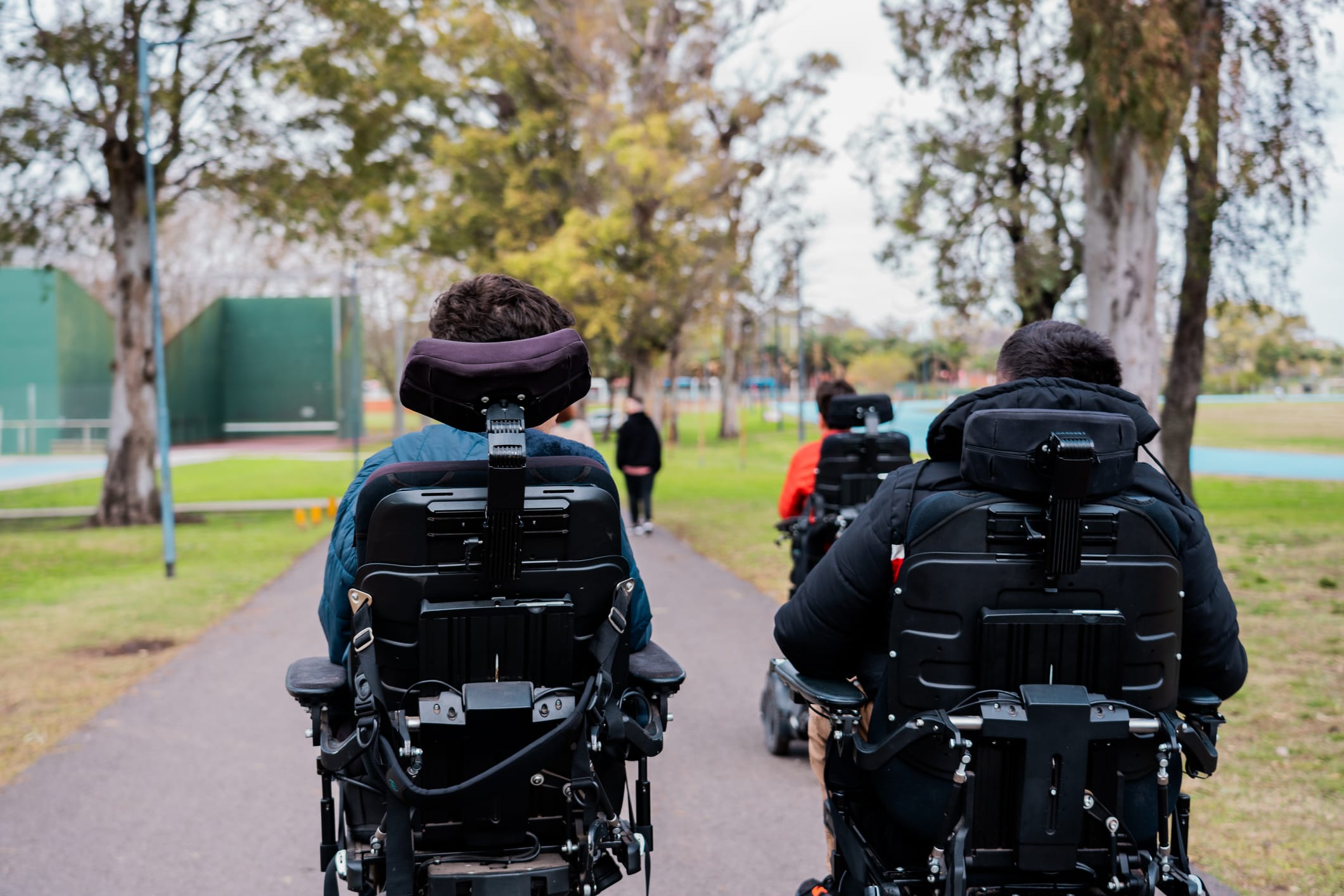 Two friends in power wheelchairs going down a path