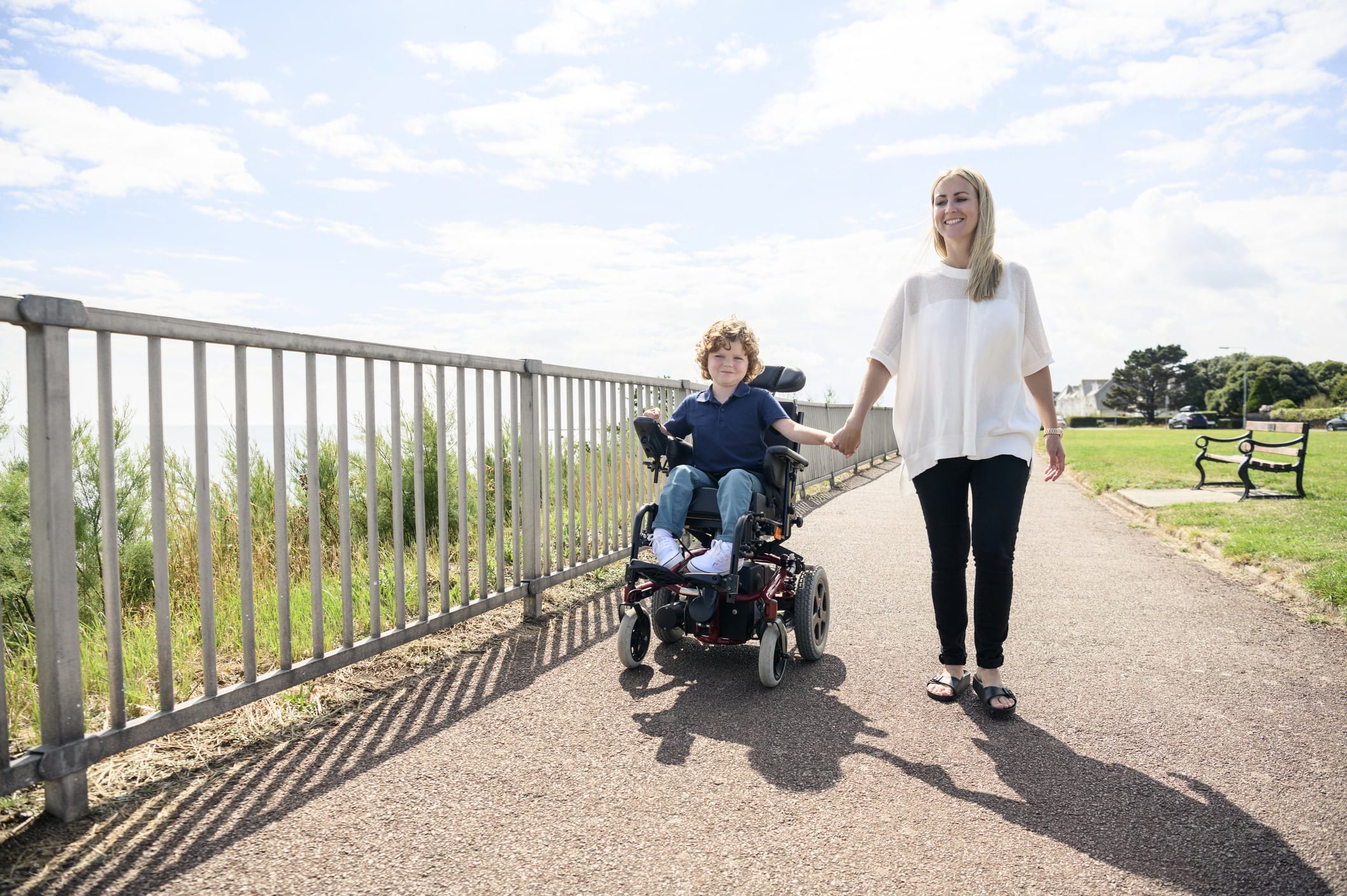 Boy in a power wheelchair outdoors with his mother